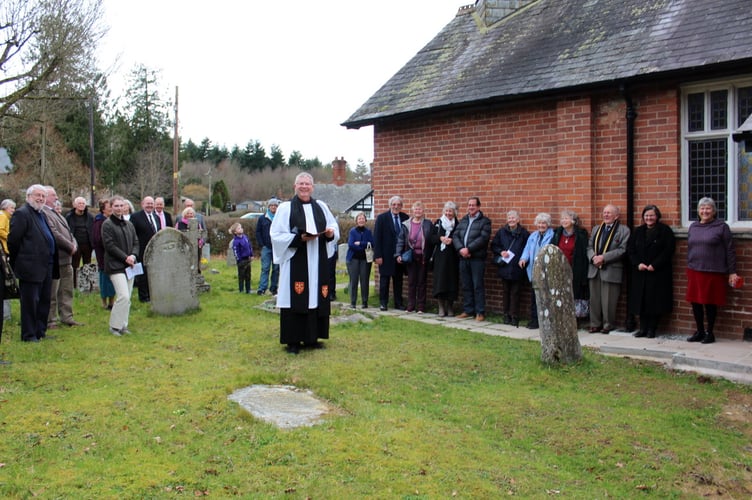 In the churchyard, people standing on the path to the toilet and on the grass with Andrew Beane the Archdeacon of Exeter.  SR 7126