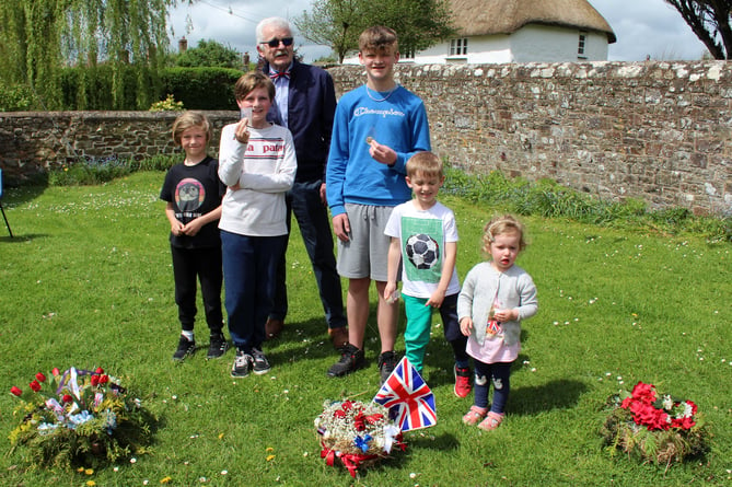 Parish Council Chairman Andrew Green presented Coronation commemorative coins to Coldridge children. In the foreground are some of the commemorative floral crowns produced by Coldridge Gardening Club.
